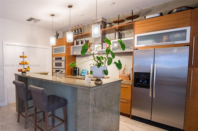 kitchen featuring pendant lighting, a breakfast bar, white appliances, a kitchen island with sink, and stone countertops