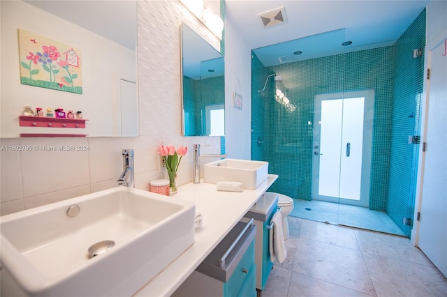 bathroom with tile patterned floors, vanity, a shower with door, tile walls, and toilet