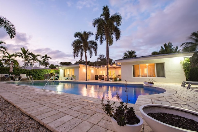 pool at dusk with pool water feature and a patio