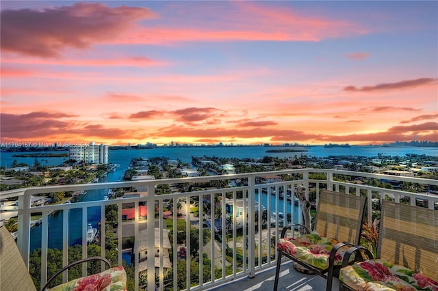 balcony at dusk featuring a water view