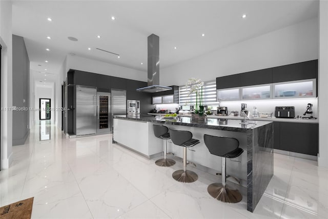 kitchen with a breakfast bar, a center island, stainless steel built in fridge, and range hood