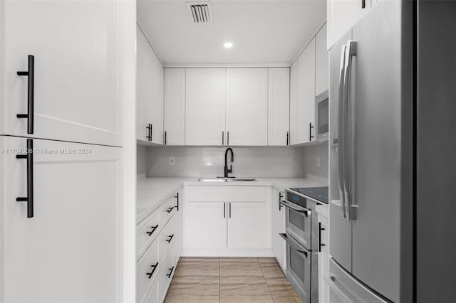 kitchen with sink, stainless steel appliances, light stone counters, decorative backsplash, and white cabinets