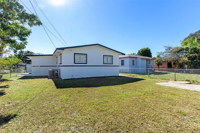 rear view of house with central AC unit and a yard