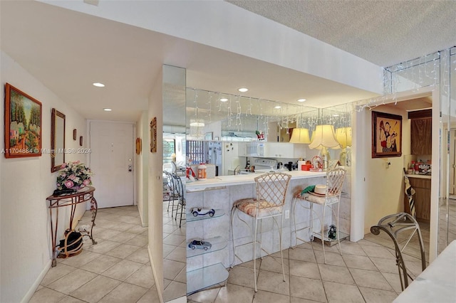 kitchen featuring a kitchen breakfast bar, kitchen peninsula, light tile patterned floors, and a textured ceiling