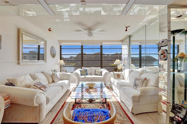 tiled living room with ceiling fan, a water view, and a textured ceiling