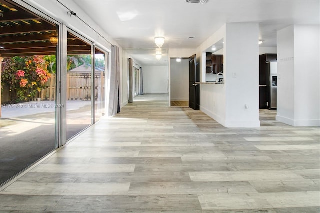 corridor with light wood-type flooring, visible vents, and baseboards