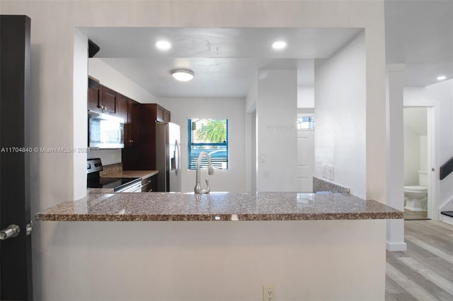 kitchen featuring appliances with stainless steel finishes, light wood-style floors, dark brown cabinets, dark stone counters, and a peninsula