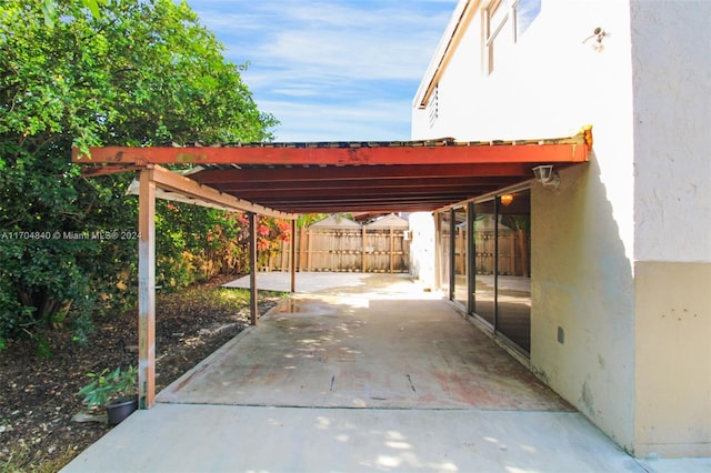 view of patio featuring driveway, an attached carport, and fence