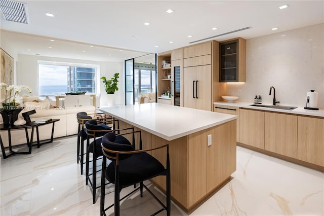 kitchen with paneled fridge, sink, light brown cabinets, a center island, and a breakfast bar area