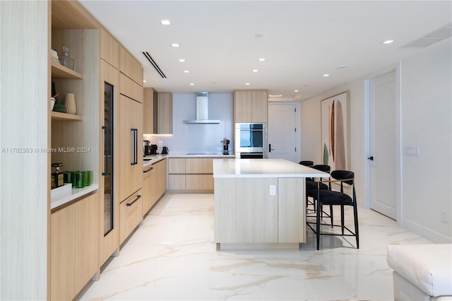 kitchen with wall chimney exhaust hood, a center island, a breakfast bar area, and light brown cabinetry