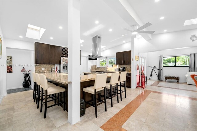 kitchen featuring ceiling fan, kitchen peninsula, a kitchen bar, island range hood, and dark brown cabinets