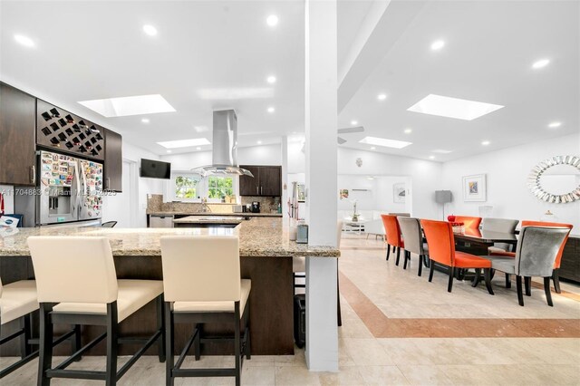 kitchen featuring stainless steel refrigerator with ice dispenser, backsplash, island exhaust hood, lofted ceiling with skylight, and a breakfast bar