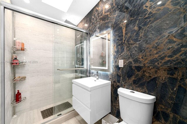 bathroom with a skylight, vanity, tile walls, toilet, and a shower with shower door