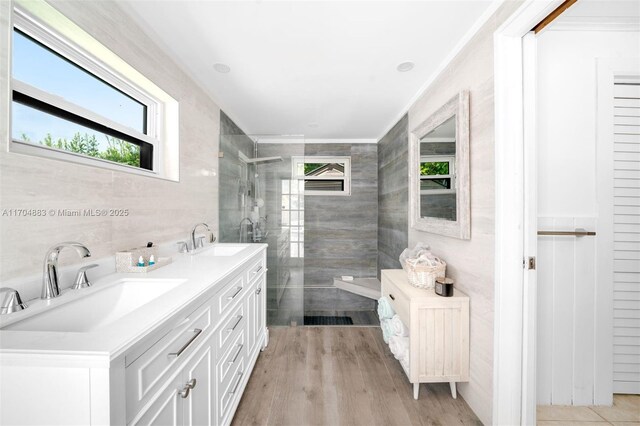 bathroom featuring ornamental molding, a tile shower, vanity, wood-type flooring, and tile walls