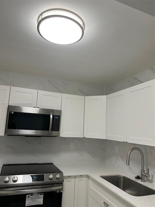 kitchen with backsplash, white cabinetry, sink, and appliances with stainless steel finishes