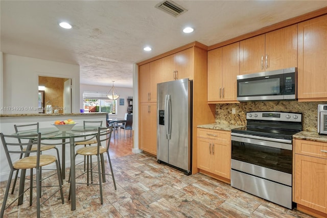 kitchen featuring light brown cabinets, a kitchen breakfast bar, decorative backsplash, light stone countertops, and appliances with stainless steel finishes