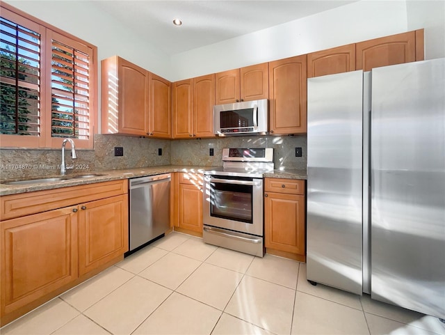 kitchen with sink, stainless steel appliances, light stone counters, decorative backsplash, and light tile patterned flooring