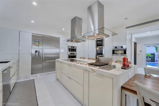 kitchen with light tile patterned floors, white cabinets, island range hood, a kitchen island, and appliances with stainless steel finishes