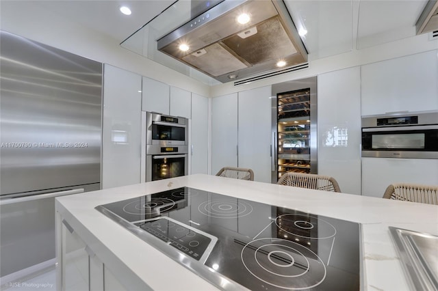 kitchen featuring a breakfast bar, wine cooler, white cabinetry, stainless steel appliances, and extractor fan