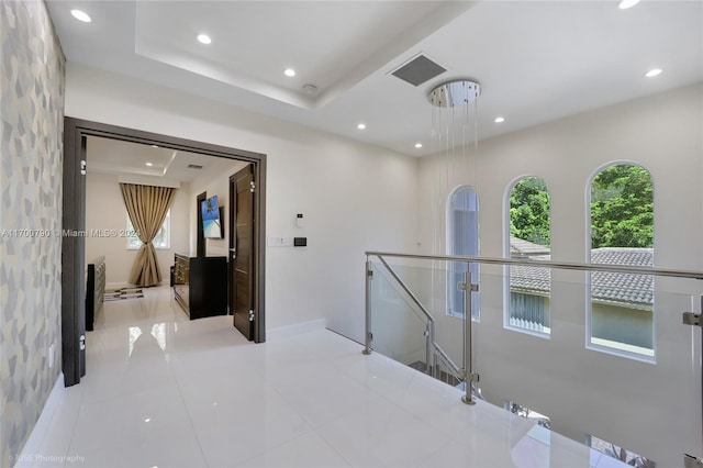 hall with a raised ceiling and light tile patterned floors