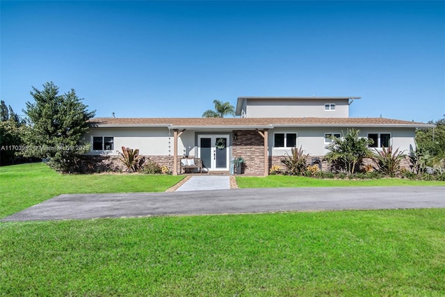 view of front of property featuring a front yard, stone siding, driveway, and stucco siding