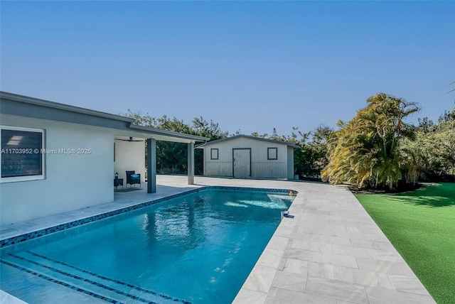 pool featuring a yard, an outbuilding, a patio, and ceiling fan