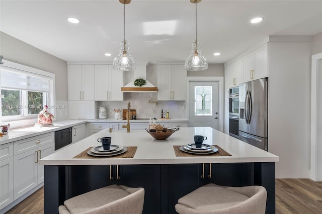 kitchen with a center island with sink, dark wood-type flooring, wall chimney range hood, and appliances with stainless steel finishes