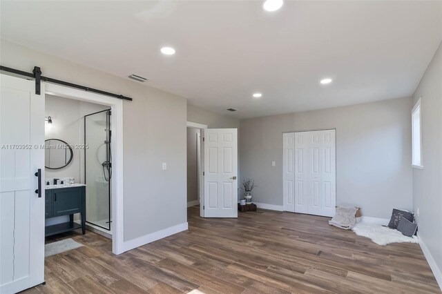 bedroom featuring connected bathroom, a closet, dark hardwood / wood-style flooring, and a barn door