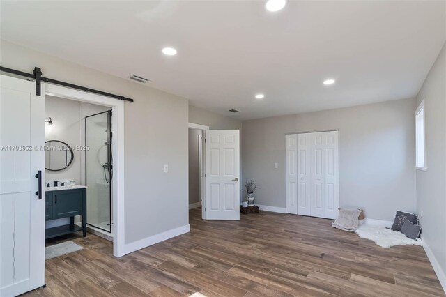 bedroom featuring baseboards, a barn door, wood finished floors, and recessed lighting