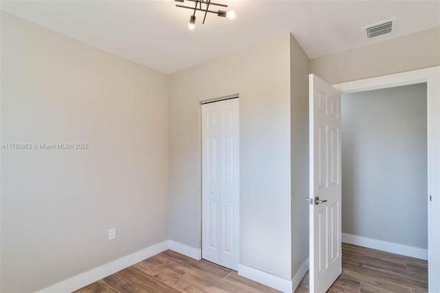 unfurnished bedroom with wood finished floors, visible vents, and baseboards