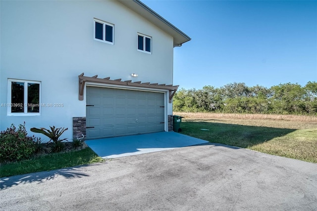 view of side of home with an attached garage, driveway, a lawn, and stucco siding