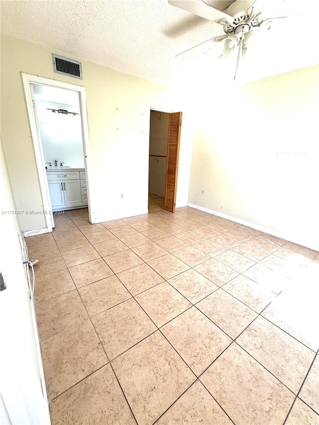 unfurnished bedroom featuring ceiling fan, sink, ensuite bathroom, a textured ceiling, and light tile patterned floors