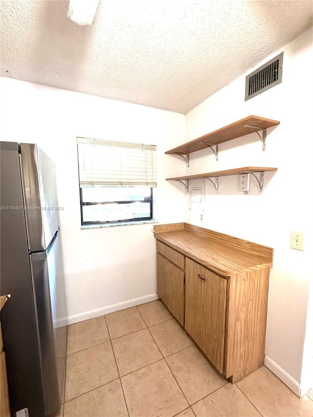 kitchen featuring stainless steel fridge, light tile patterned flooring, and a textured ceiling