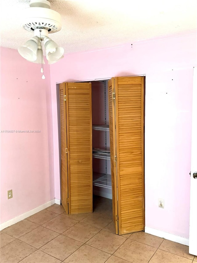 unfurnished bedroom featuring tile patterned flooring, a textured ceiling, a closet, and ceiling fan