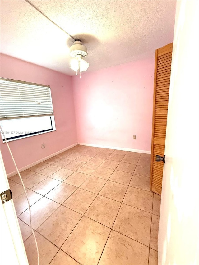 spare room featuring ceiling fan, light tile patterned flooring, and a textured ceiling