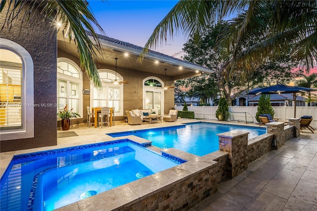 pool at dusk featuring an in ground hot tub, an outdoor hangout area, and a patio area