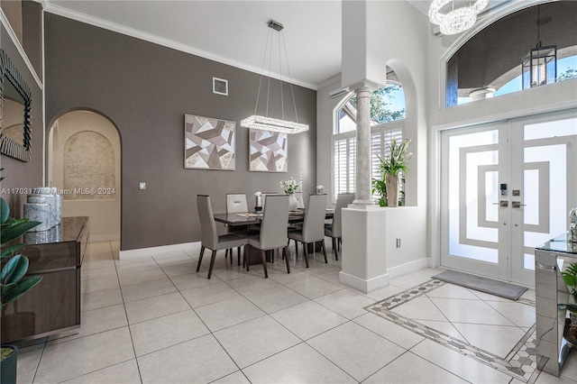 dining area featuring decorative columns, crown molding, a towering ceiling, a chandelier, and light tile patterned floors