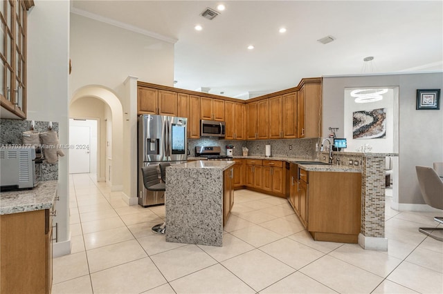 kitchen with light tile patterned flooring, crown molding, light stone countertops, appliances with stainless steel finishes, and a kitchen island