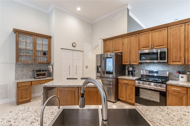 kitchen with backsplash, light stone counters, stainless steel appliances, crown molding, and light tile patterned flooring