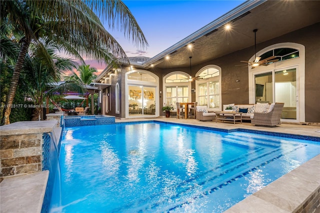 pool at dusk featuring an in ground hot tub, an outdoor hangout area, pool water feature, ceiling fan, and a patio area