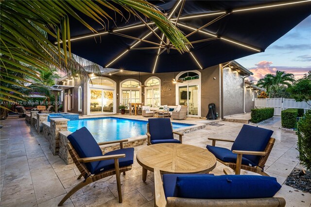 pool at dusk with an in ground hot tub, a patio, and an outdoor hangout area