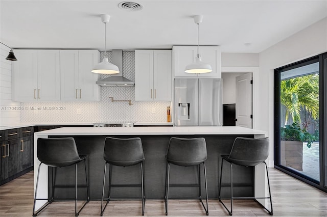 kitchen with wall chimney exhaust hood, pendant lighting, white cabinets, stainless steel fridge with ice dispenser, and a kitchen island