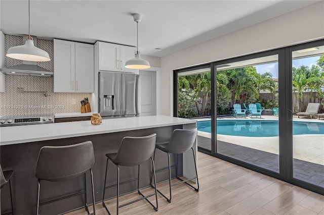 kitchen with white cabinetry, backsplash, decorative light fixtures, appliances with stainless steel finishes, and light wood-type flooring