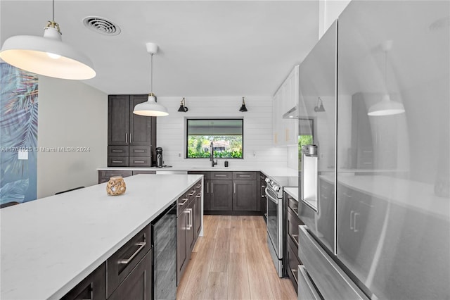 kitchen with appliances with stainless steel finishes, light wood-type flooring, sink, decorative light fixtures, and wine cooler