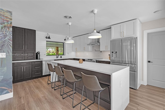 kitchen with white cabinetry, a center island, stainless steel appliances, light hardwood / wood-style flooring, and a breakfast bar