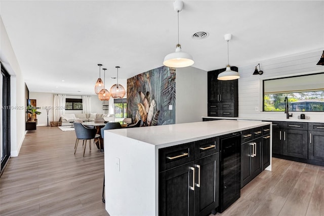 kitchen featuring a kitchen island, light hardwood / wood-style flooring, beverage cooler, and a healthy amount of sunlight