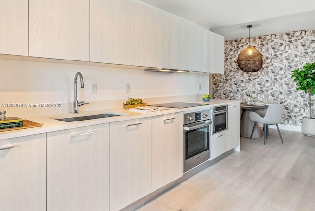 kitchen with light wood-type flooring, black electric cooktop, sink, oven, and hanging light fixtures