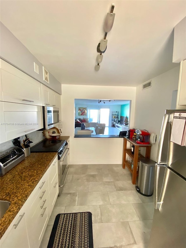 kitchen with white cabinets, appliances with stainless steel finishes, and dark stone counters