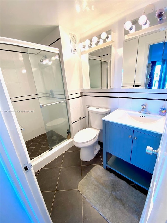 bathroom featuring tile patterned flooring, toilet, a shower with shower door, and tile walls