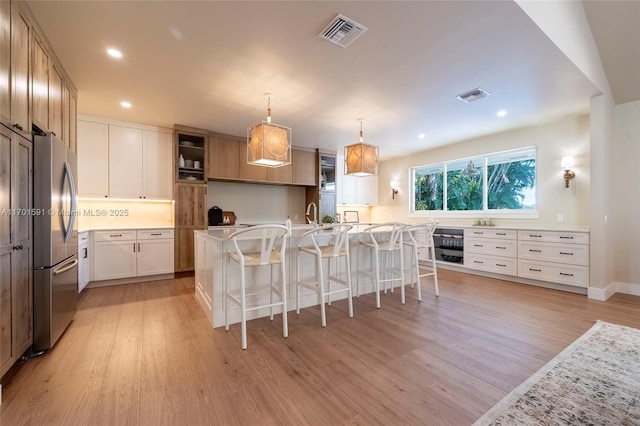 kitchen featuring a breakfast bar area, hanging light fixtures, stainless steel refrigerator, an island with sink, and light hardwood / wood-style floors